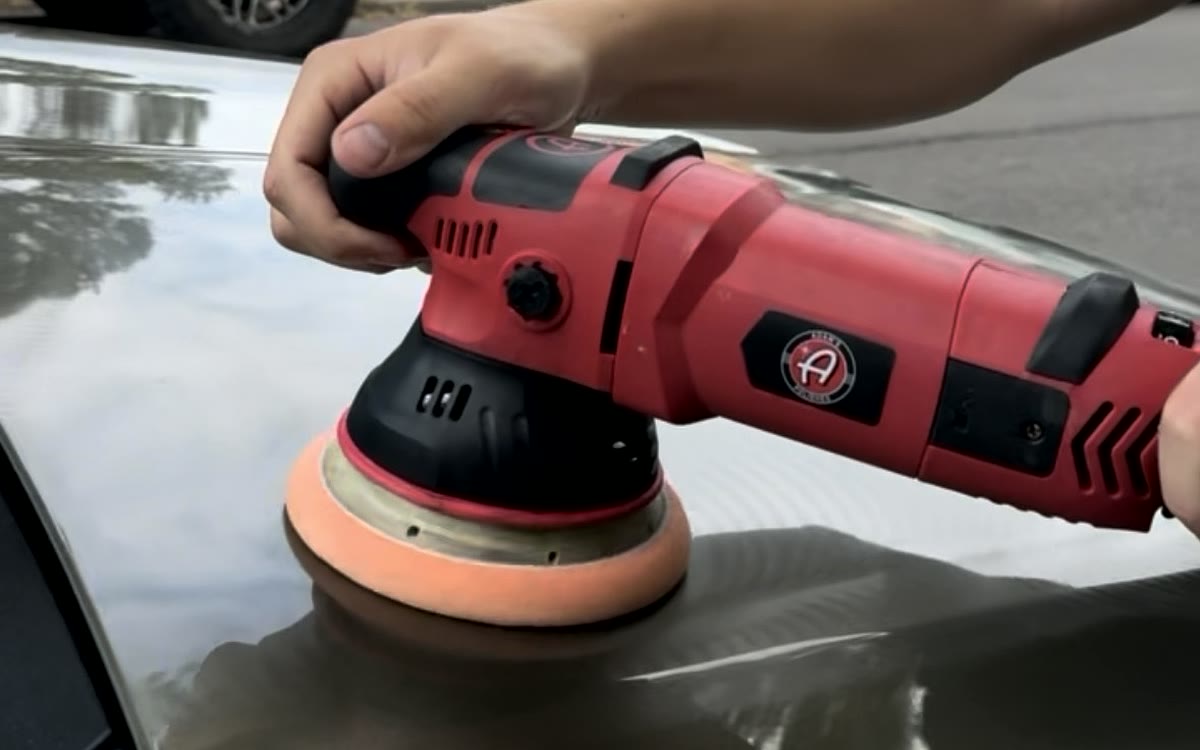 A dual-action polisher being run across glossy black paint